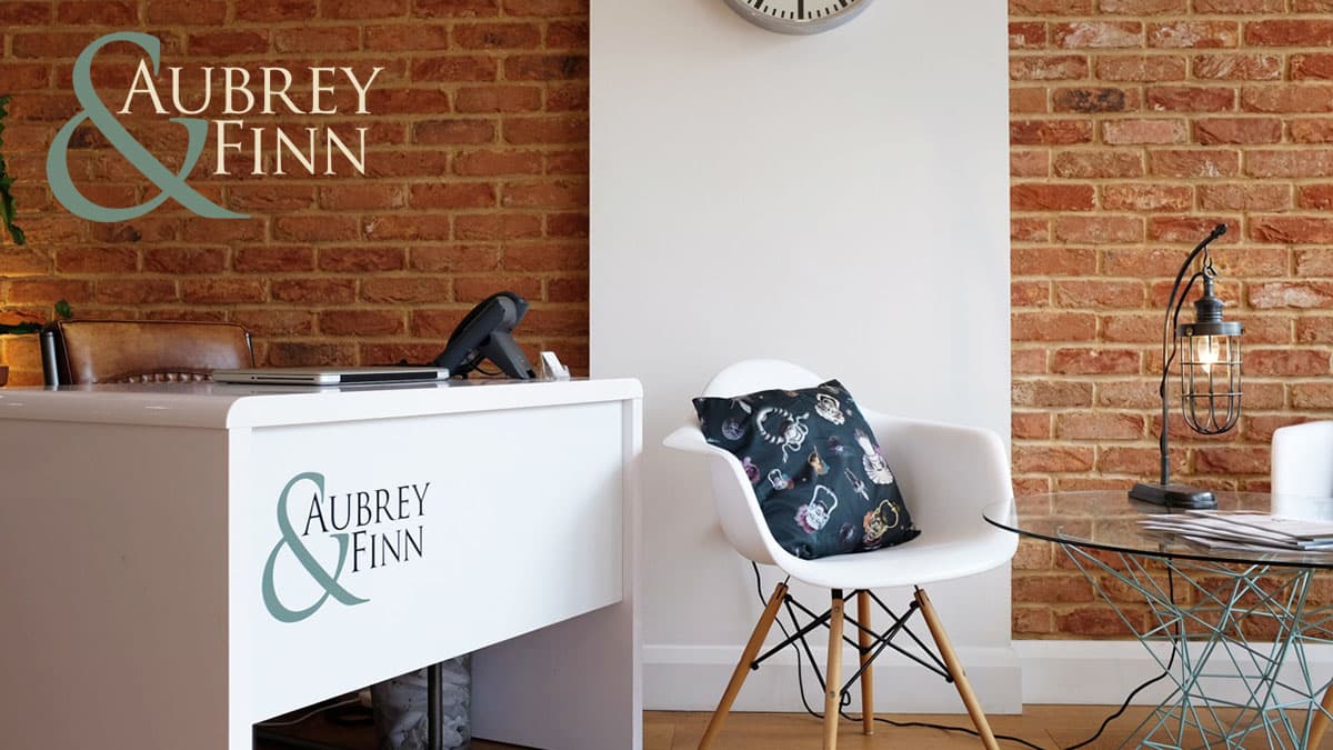 Inside the Aubrey & Finn office: a white reception desk with the logo, against exposed brick